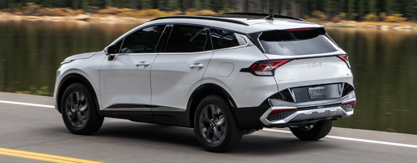 White 2023 Kia Sportage Hybrid driving past a lake