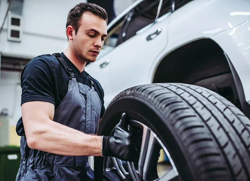 Technician examines a tire mounted on a white vehicle's wheel well in a service bay