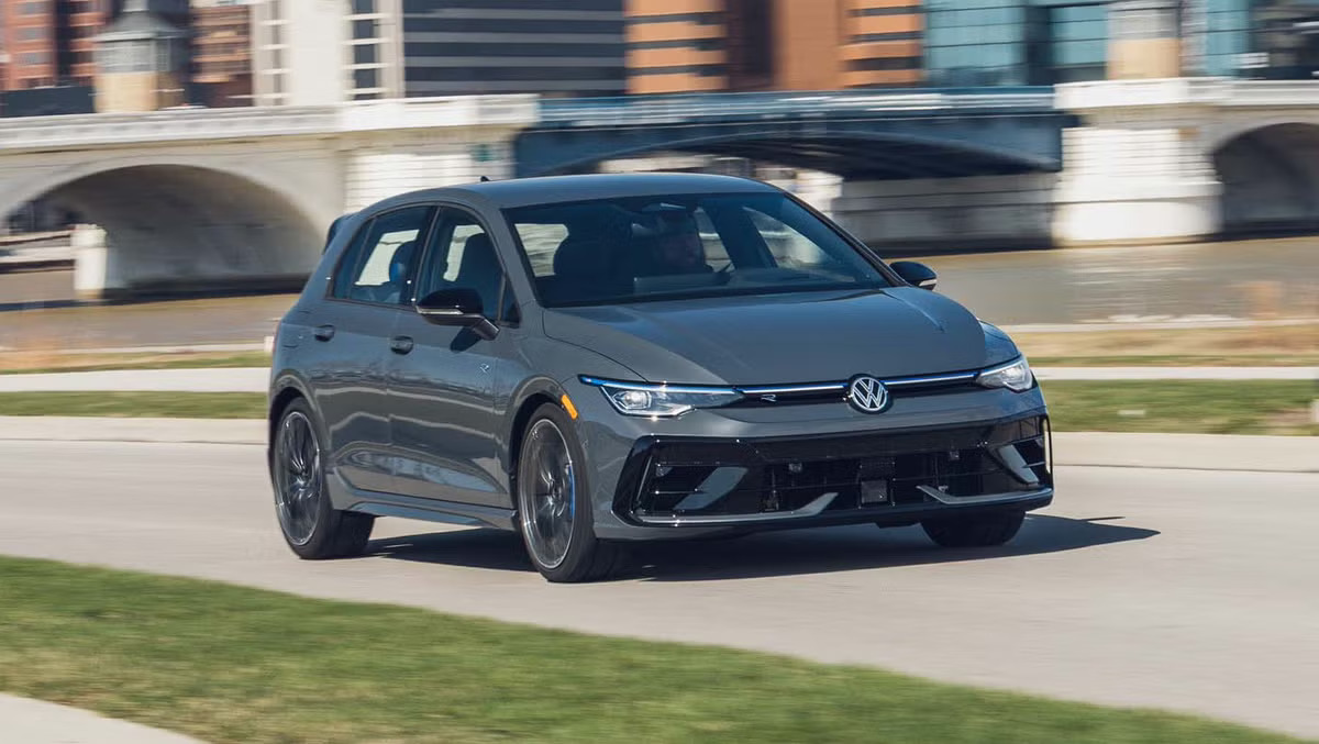 2027 Volkswagen Golf R in gray driving past a riverfront, front three-quarter view