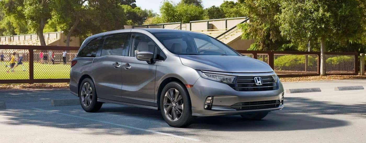 A silver 2022 Honda Odyssey Elite is shown parked in front of a soccer field.