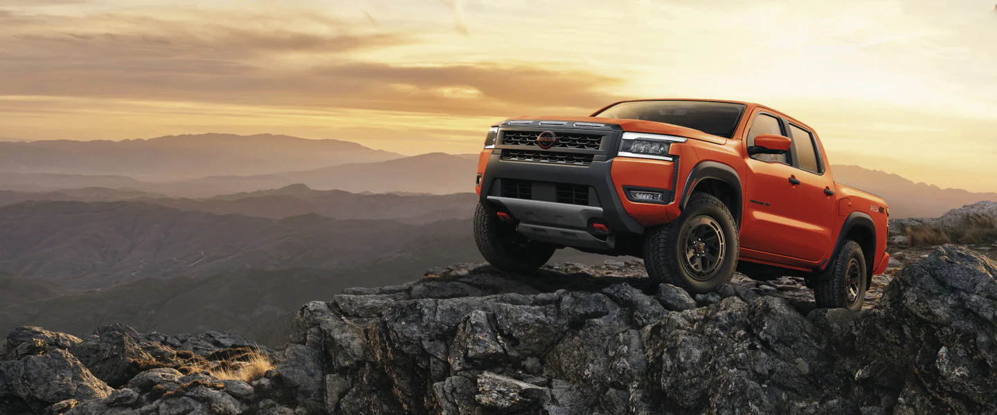 2027 Nissan Frontier PRO-4X in orange parked on a rocky mountain summit at sunset