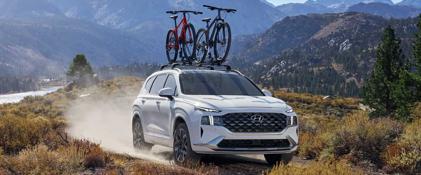 a white suv with 2 bikes on top driving in the mountains