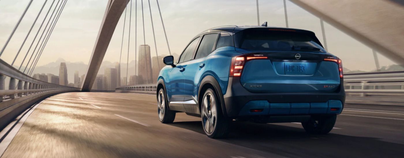 Rear view of a blue 2026 Nissan Kicks SR driving over a bridge.