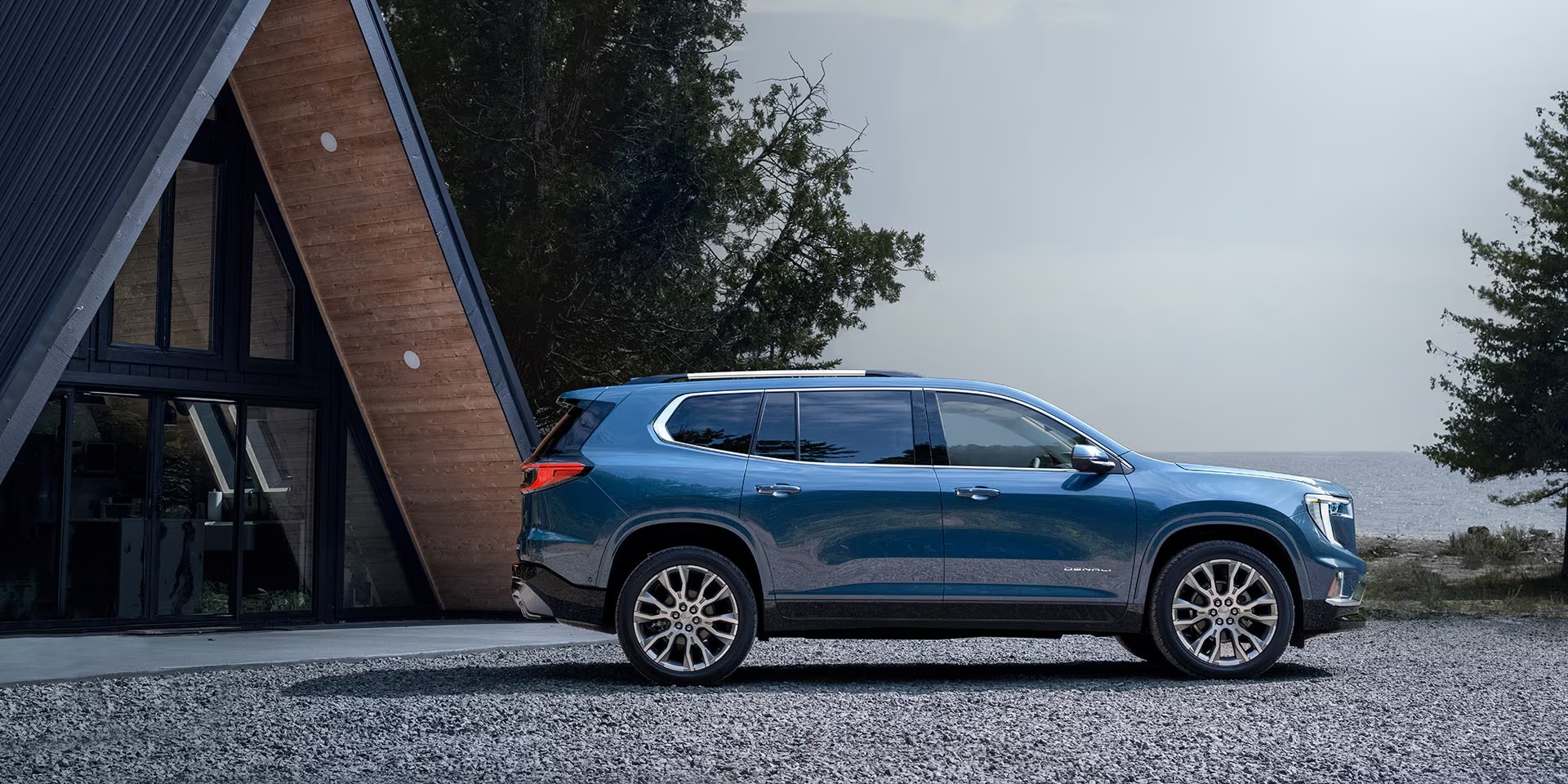Blue 2026 GMC Acadia parked outside of an A-frame cabin on a gravel driveway