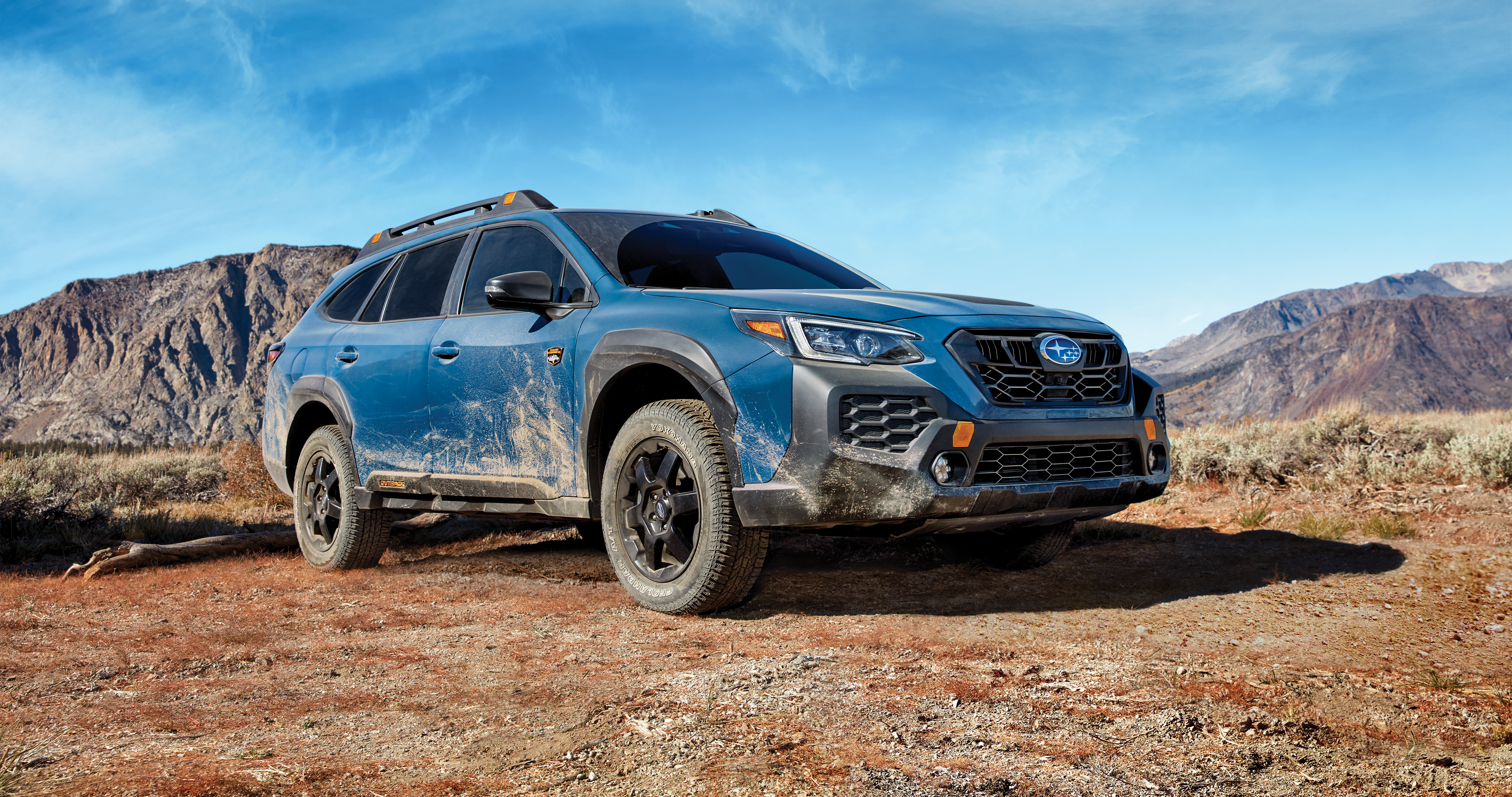 A blue Subaru Outback parked in front of mountains. 