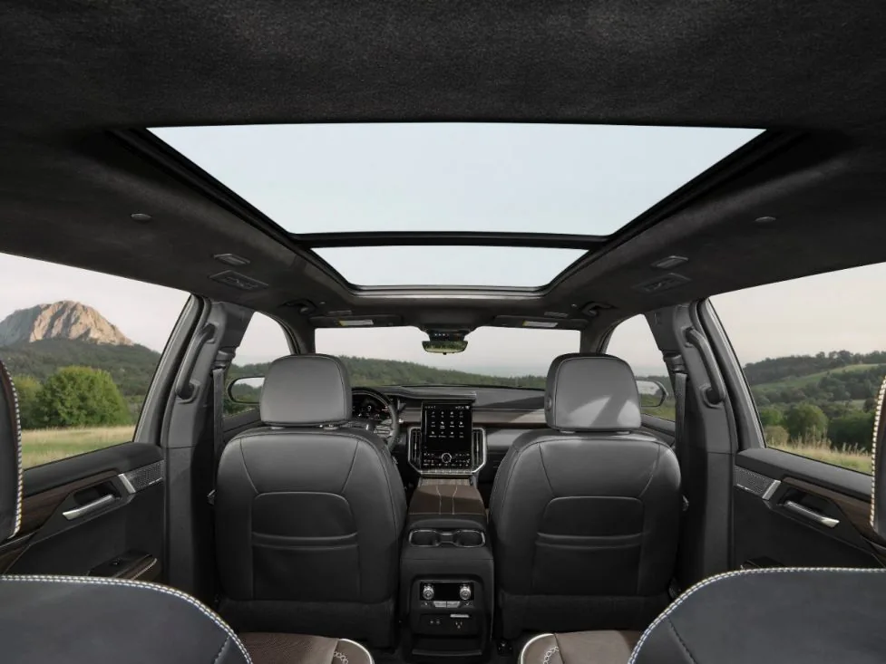Interior view of a GMC SUV's panoramic sunroof and second-row seats, with green hills visible through the windows