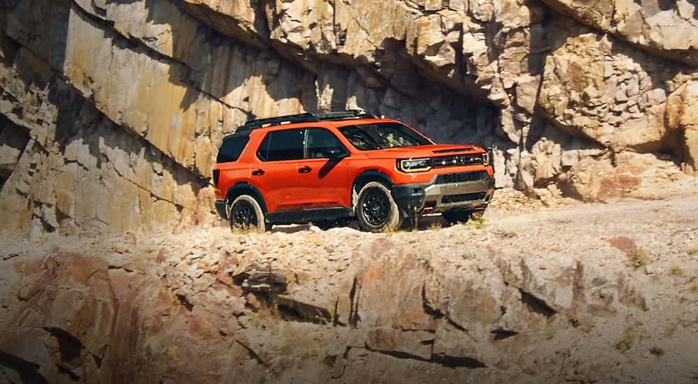 Wide angle shot of an orange 2026 Honda Passport TrailSport Elite driving by a cliffside.