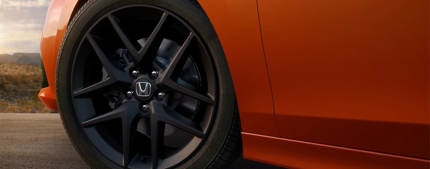 Close up shows a rim and tire of an orange 2022 Honda Civic Si