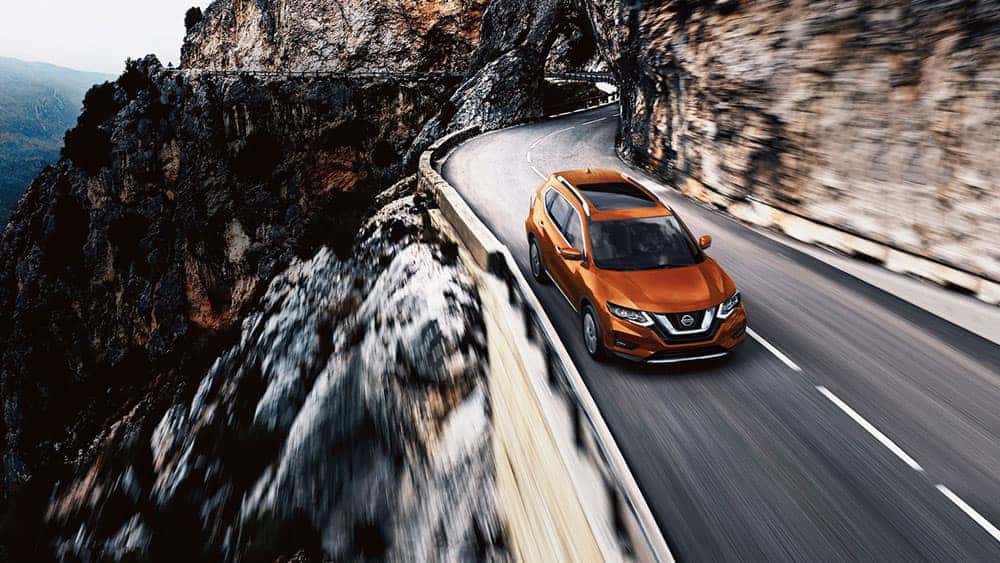 Orange 2017 Nissan Rogue driving along a cliffside mountain road