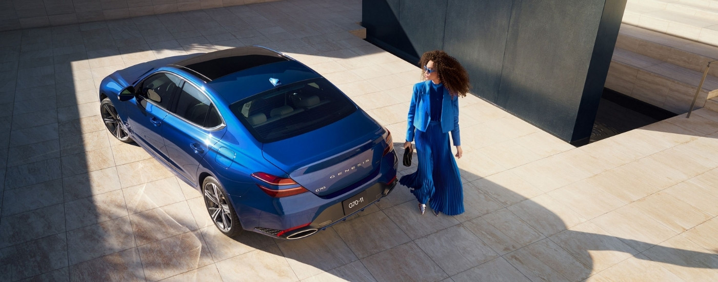 Person walking past a blue 2026 Genesis G70.