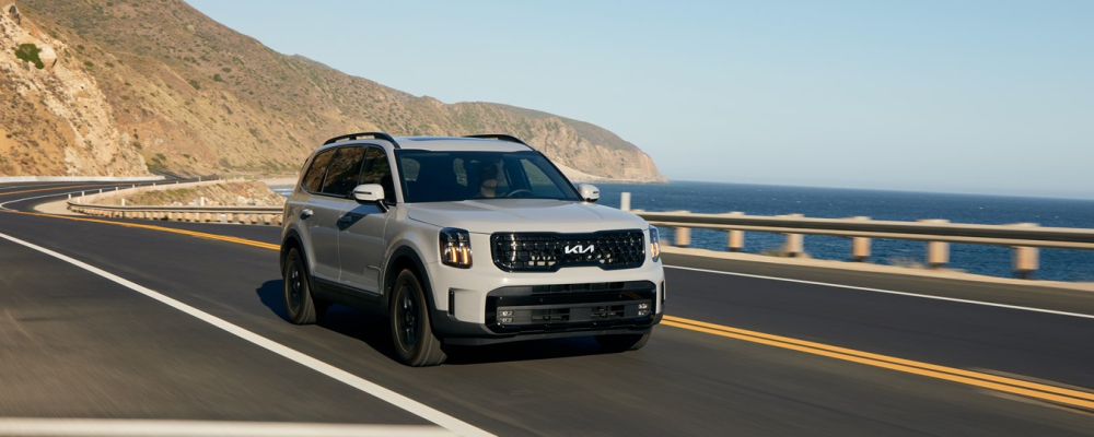 2024 Kia Telluride driving along a coastal road, showcasing its sleek design and performance features against a scenic backdrop.