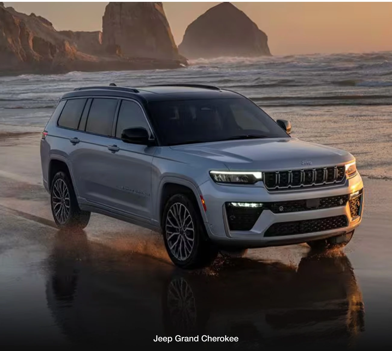 Jeep Grand Cherokee drives along a serene beach at sunset, with dramatic cliffs in the background.