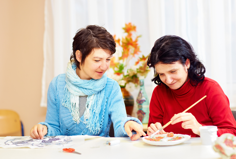 Caretaker (left) helps woman (right) with her painting