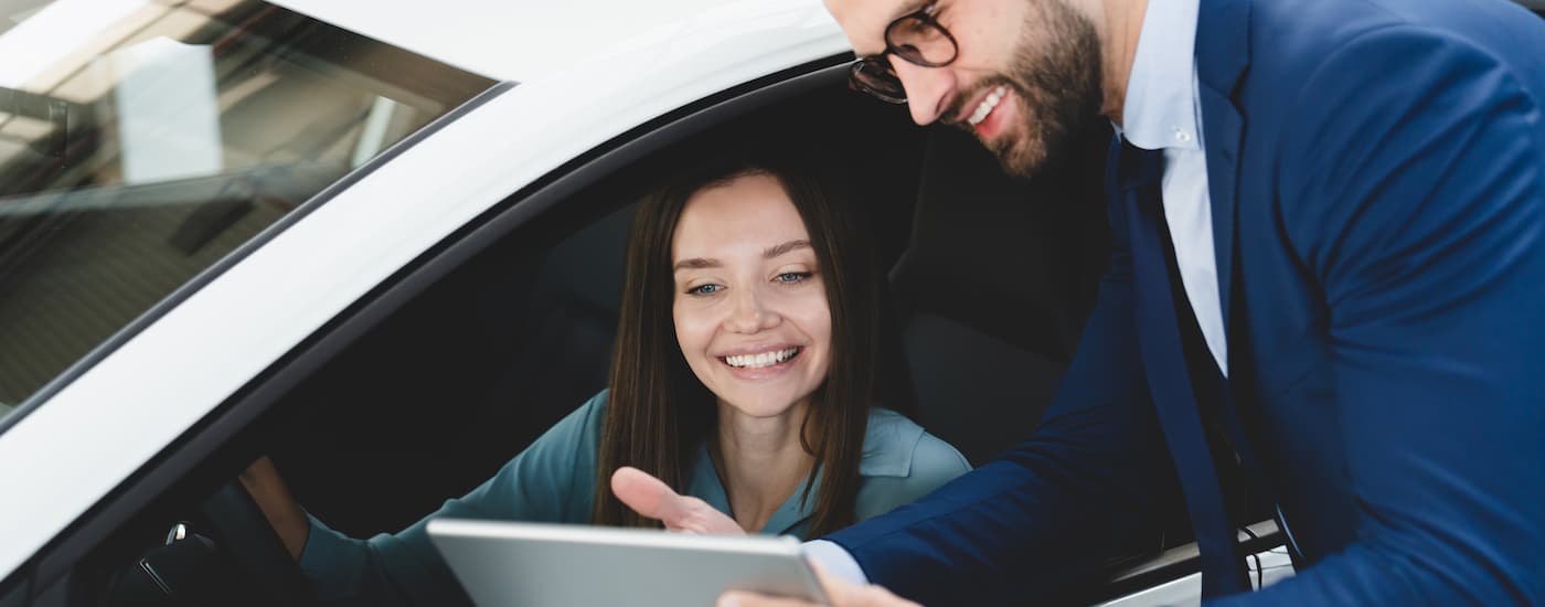 A salesman is speaking to a customer sitting in a car.