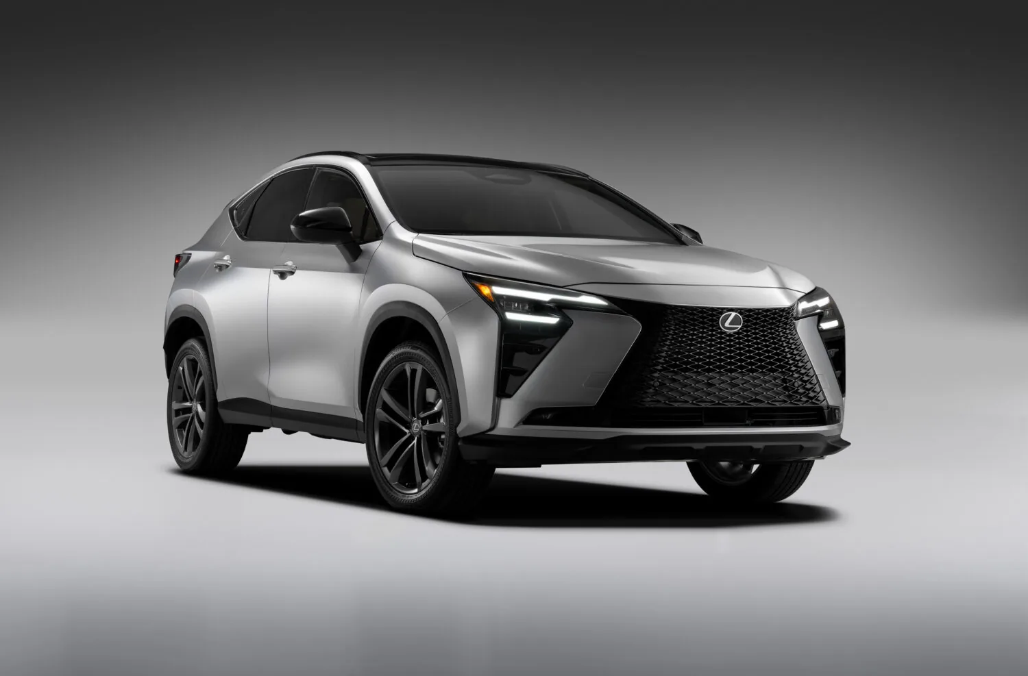 Point-of-view from the driver's seat of a Lexus showing hands on the steering wheel with the Lexus logo, a digital speedometer reading 60 mph, and an infotainment screen displaying a music playlist, with a sunset over a winding road ahead.