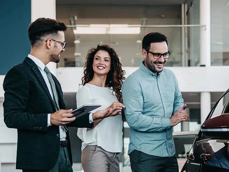 Smiling couple and car salesman talking inside a bright modern dealership showroom