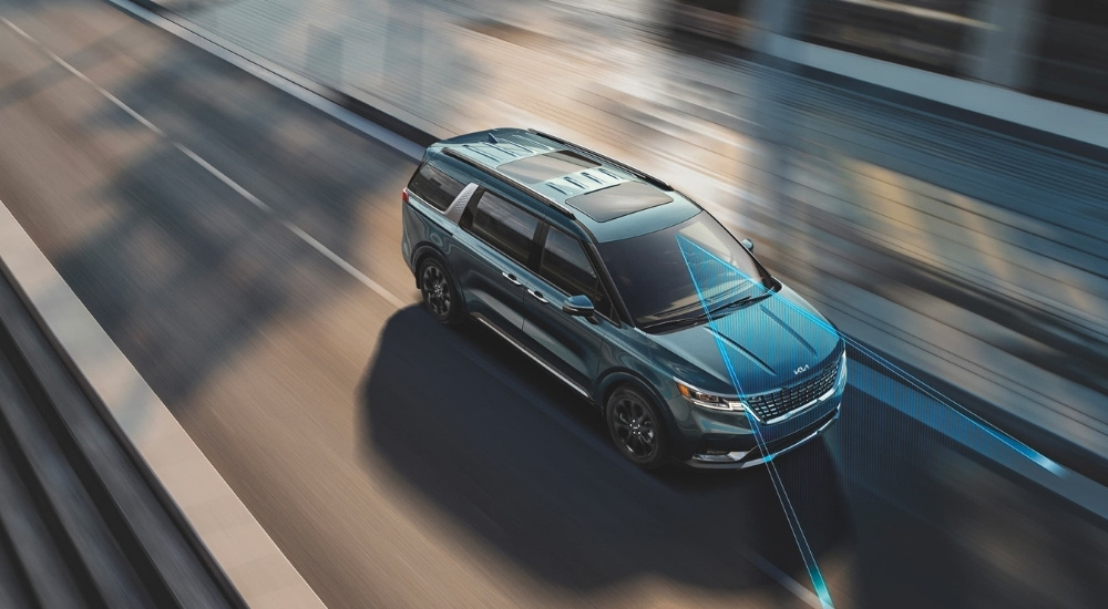 Blue 2023 Kia Carnival is shown driving on a highway