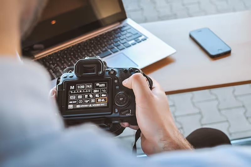 Hands holding a digital camera next to a laptop