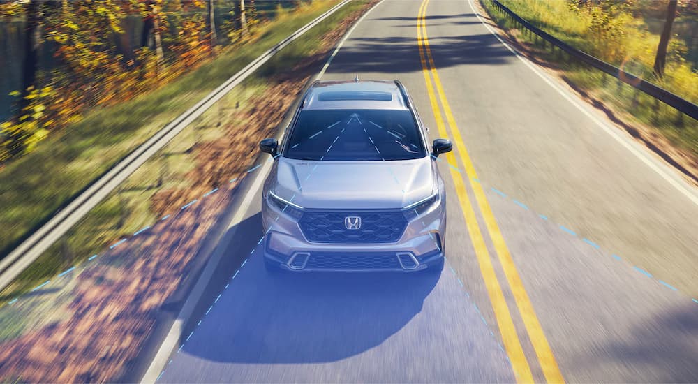 White 2026 Honda CR-V Sport Touring Hybrid driving down a road