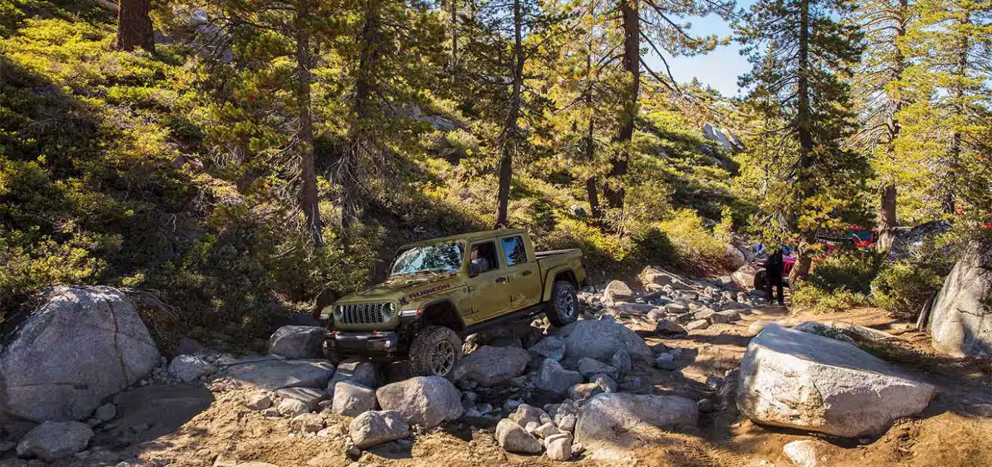 A green jeep driving over some rocks.