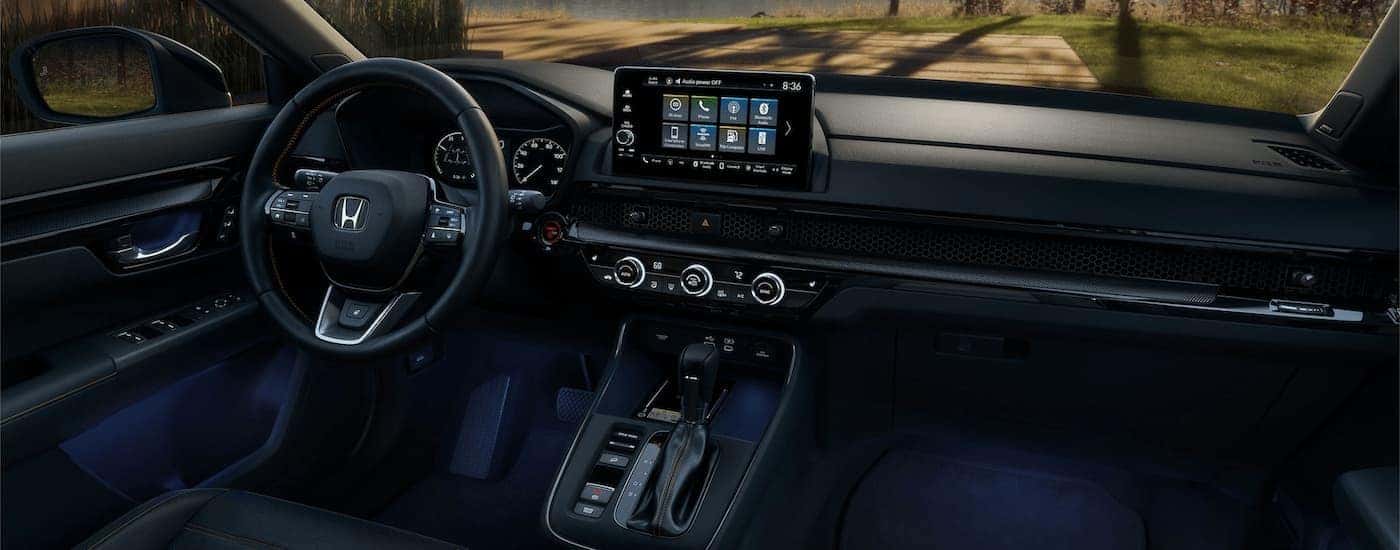 The black interior of a 2023 Honda CR-V Sport Touring shows the steering wheel and center console.