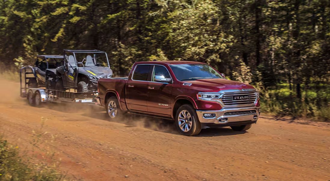 red 2023 RAM 1500 EcoDiesel tows trailer with a gator down a dirt road