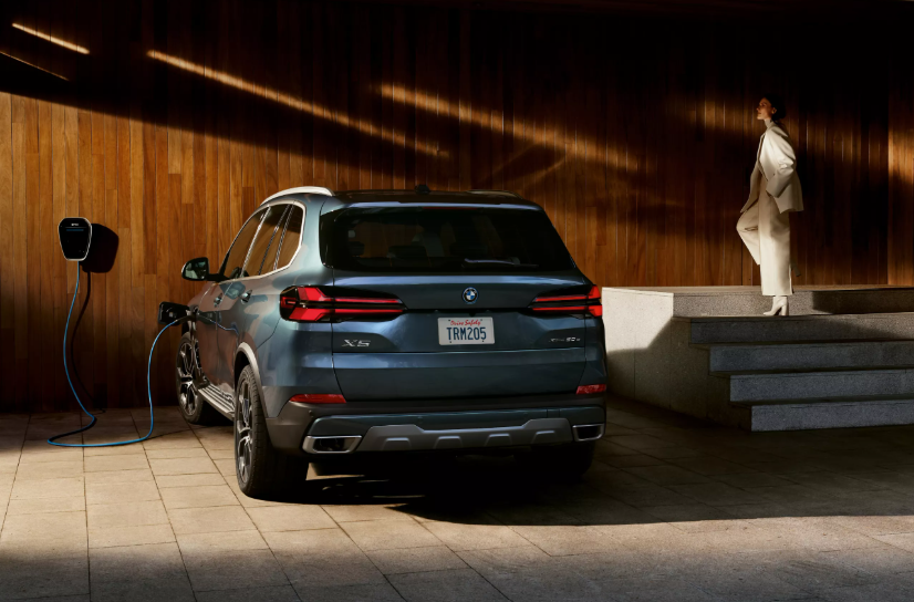 A BMW X5 plug-in hybrid charging with a woman wearing white standing on stairs next to it