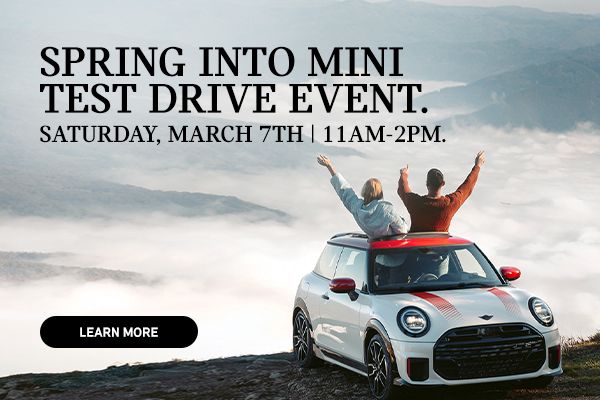 White MINI 2 Door on top of a mountain with 2 people sticking out of the sun roof.