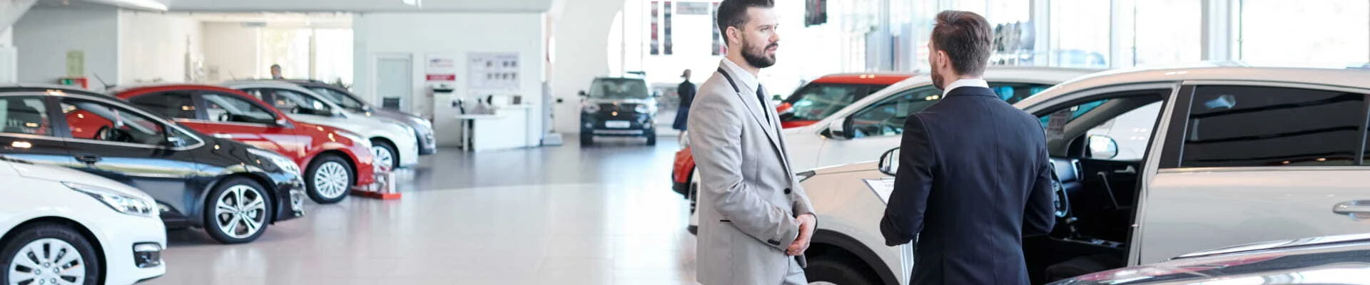 Two sales representatives talking beside a vehicle inside a car dealership showroom.