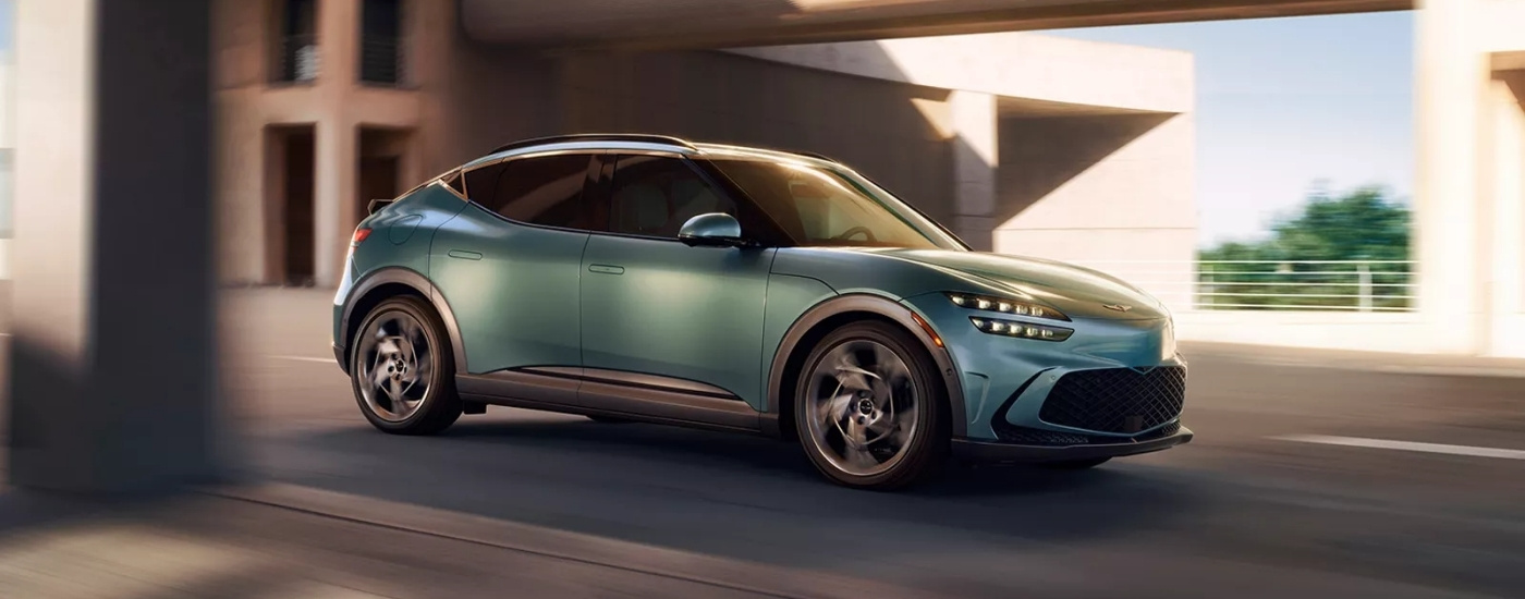 A blue 2025 Genesis GV60 driving down a street.