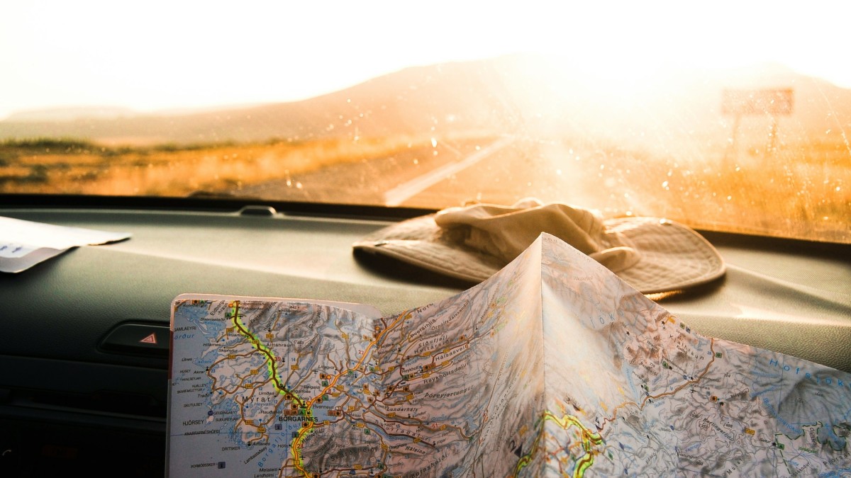 Map and Hat on Dashboard of Vehicle on Road Trip in Summer