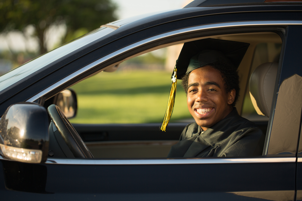 graduate dressed in cap and gown drives their new car