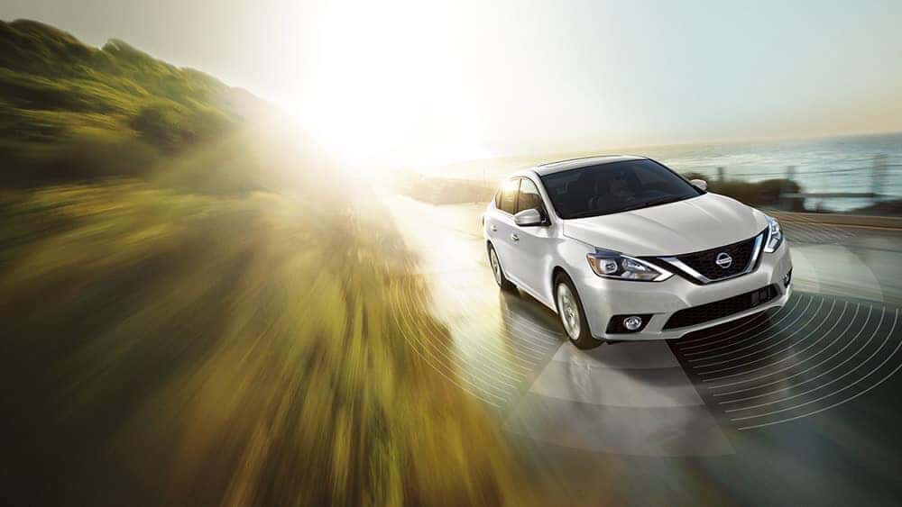 White 2018 Nissan Sentra driving on a coastal road at sunset
