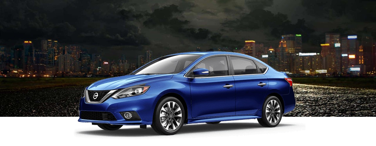 Blue 2018 Nissan Sentra sedan in front of a city skyline at night