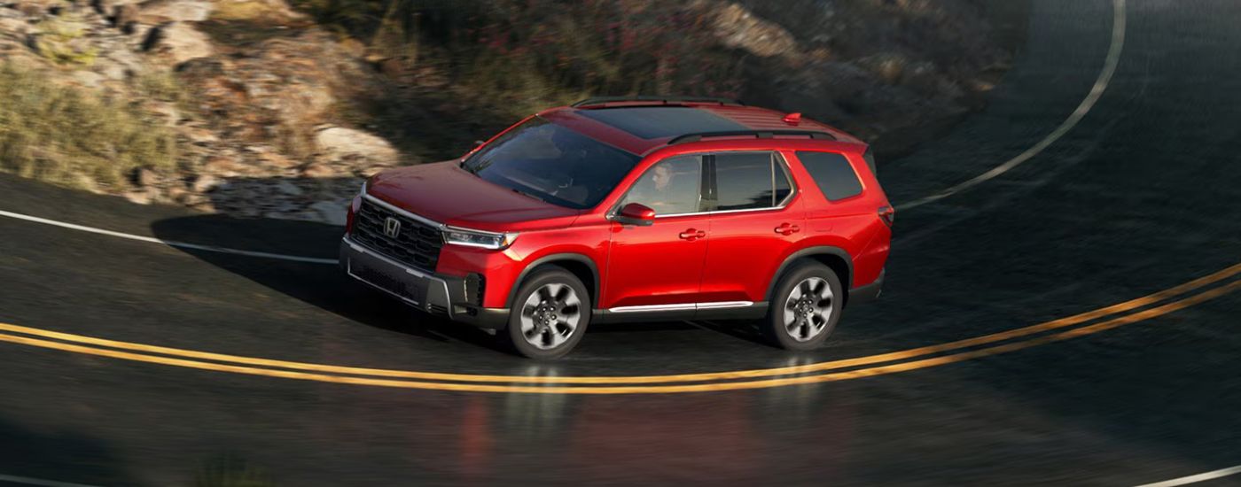 Red 2026 Honda Pilot driving on a paved road.