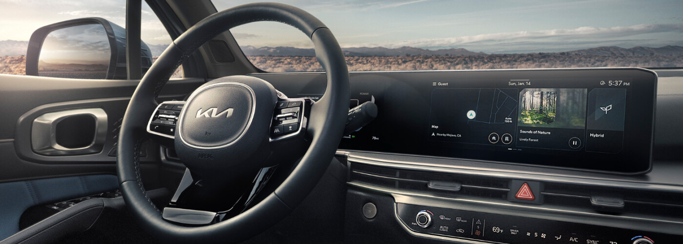 Kia Sorento Hybrid interior showcasing steering wheel and advanced infotainment system with scenic backdrop, highlighting spacious and modern design features.