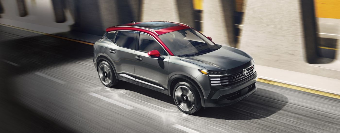 Grey 2026 Nissan Kicks with red accents driving down a paved road.