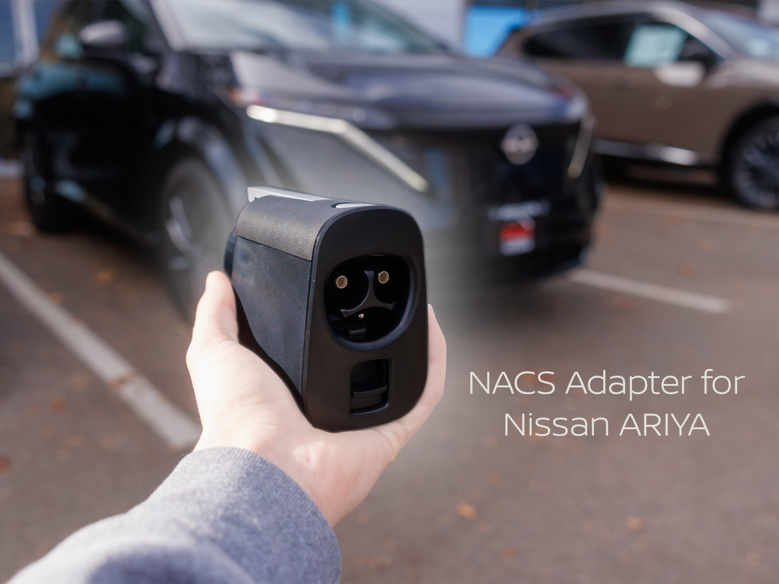 Black NACS adapter being held in hand in front of a black Nissan ARIYA with text on image stating "NACS Adapter for Nissan ARIYA."