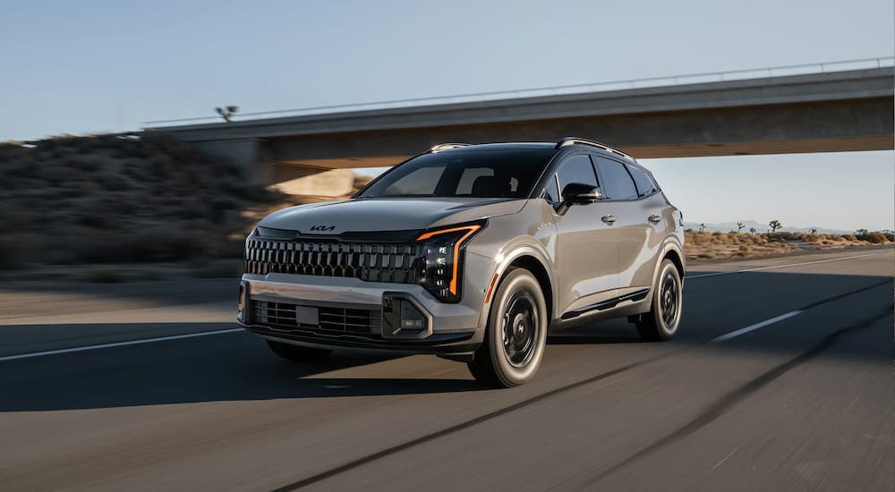 Grey 2026 Kia Sportage driving down an open road.