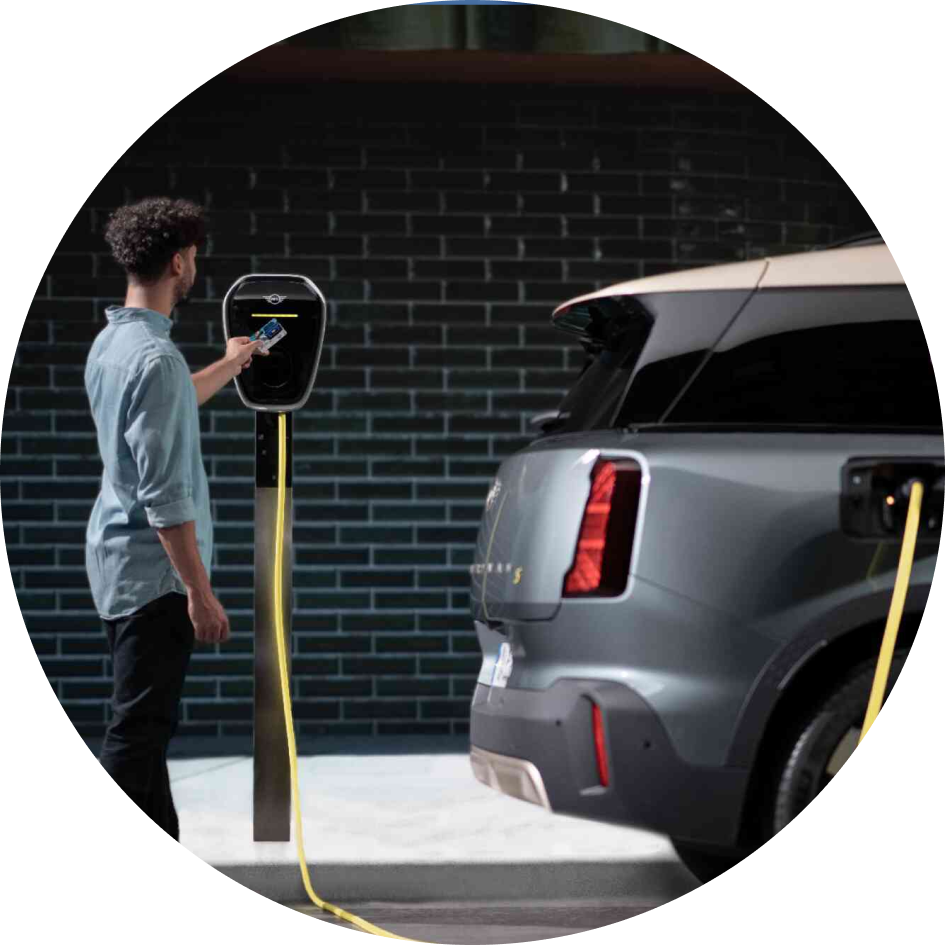 Side-view of a person charging their MINI Countryman SE ALL4 against a brick wall. 