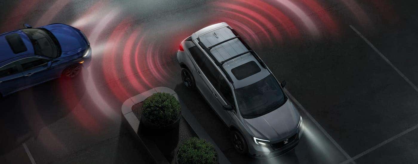 "A silver 2019 Honda Passport is shown backing up with red simulated warning lines from the blind spots.