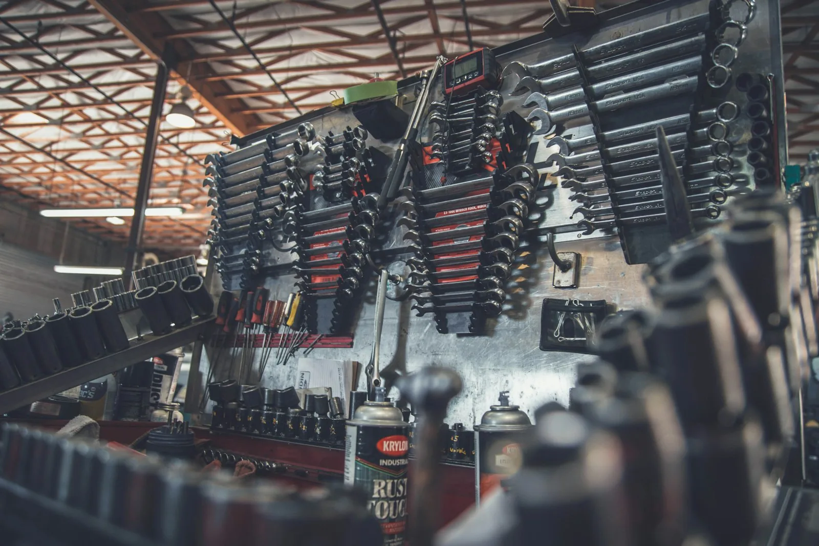 Wall-mounted racks of combination wrenches and sockets in a garage workshop with an exposed wood and steel ceiling, and a can of Krylon Industrial Rust Tough spray paint in the foreground.