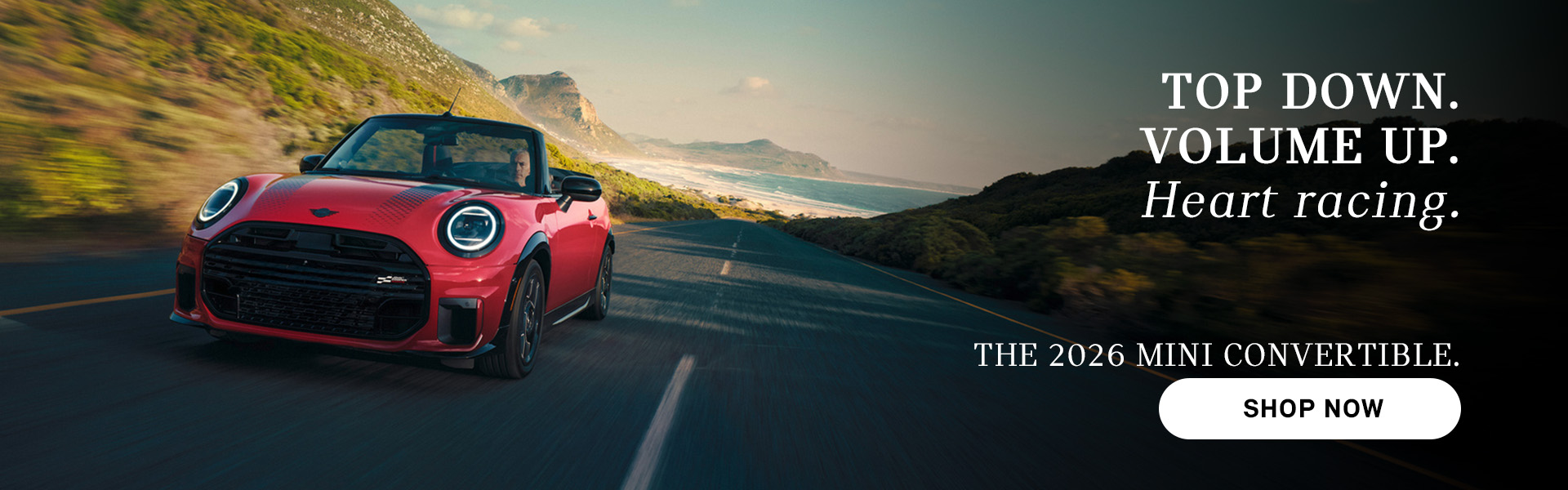 Red MINI convertible driving along a coastal road with mountains and ocean in the background, with advertisement text promoting the 2026 Mini Convertible and a “Shop Now” button.