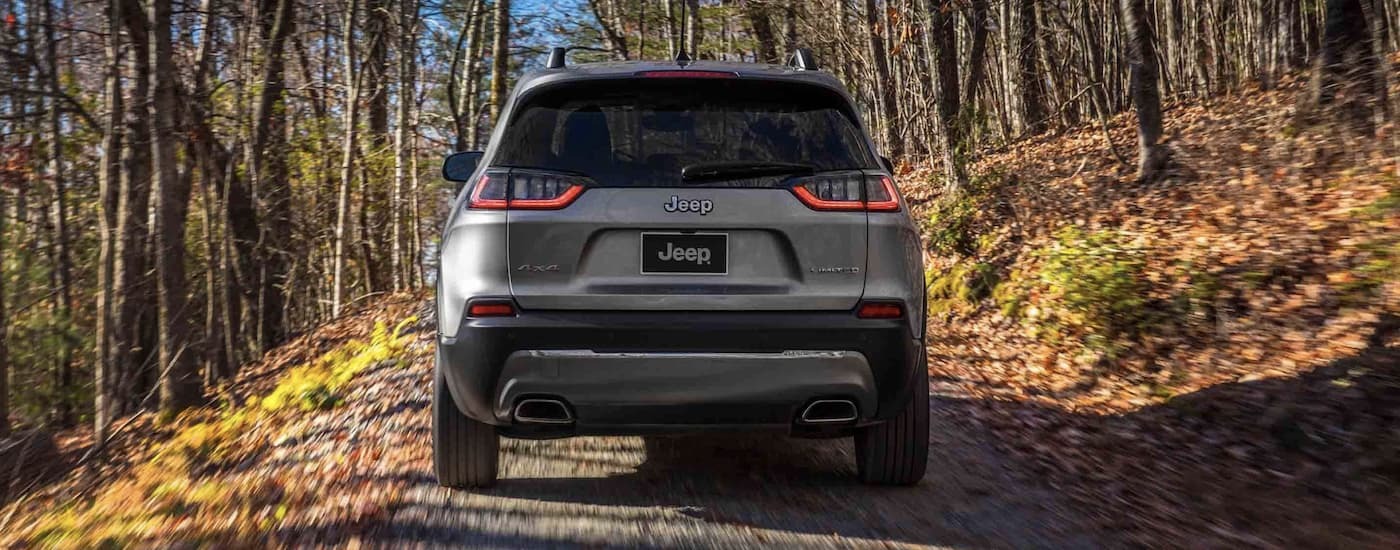 Rear of a grey 2022 Jeep Cherokee driving on a dirt road through trees