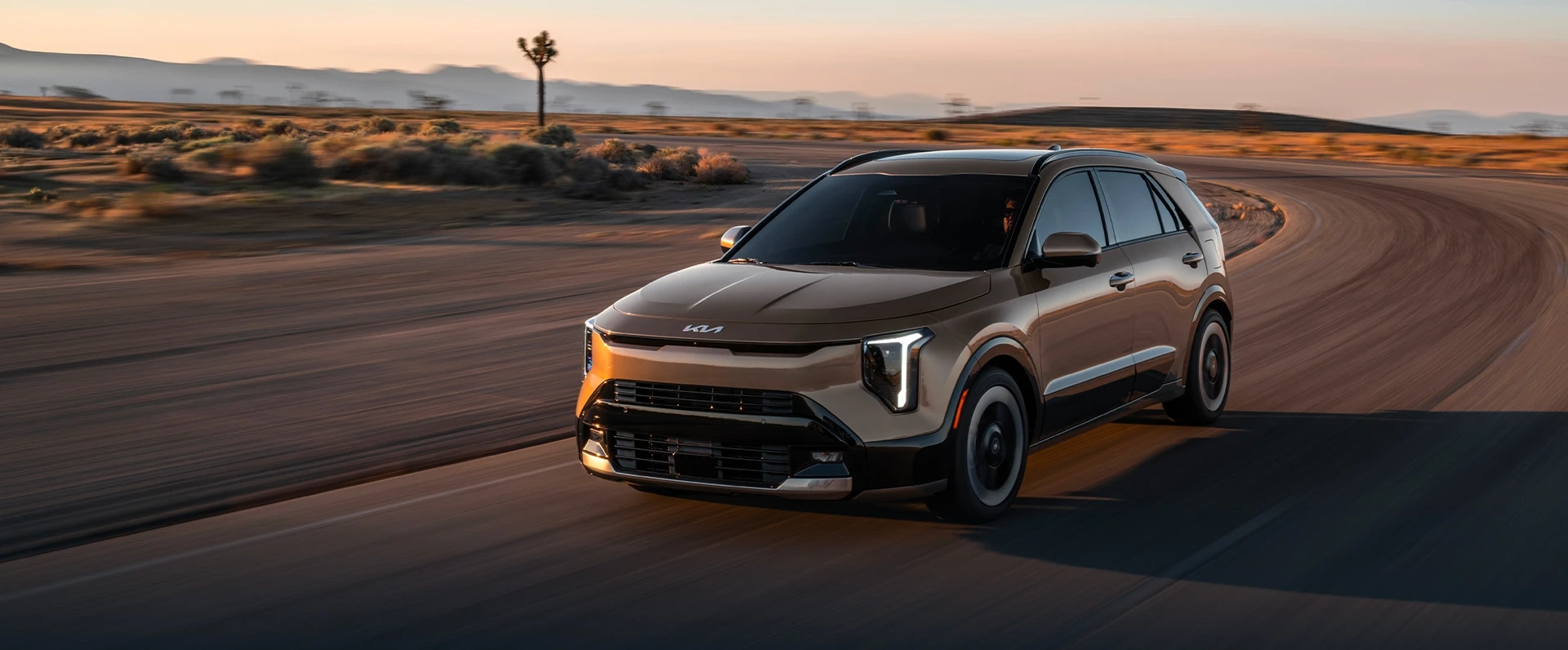 2027 Kia Niro HEV in champagne bronze driving on a desert road at sunset, front three-quarter view
