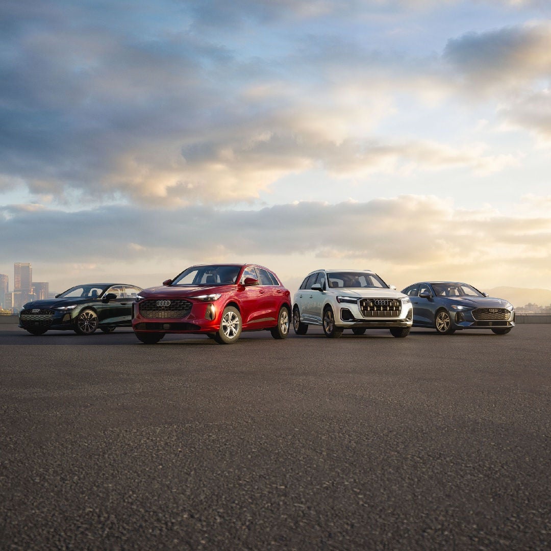 Four Audi vehicles parked side by side with a city skyline in the background.