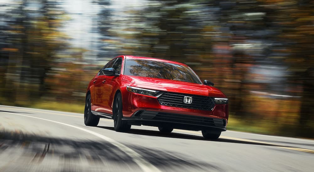 Red 2025 Honda Accord Sport-L Hybrid driving down an open road.