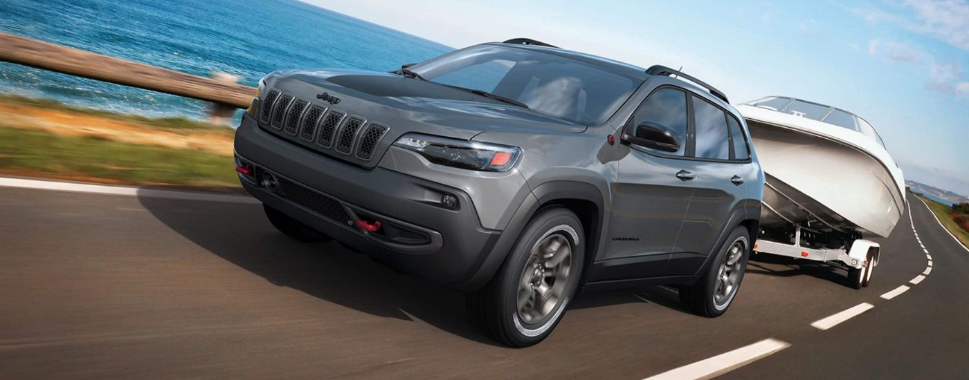 A grey 2023 Jeep Cherokee Trailhawk is shown towing a boat after leaving a Jeep dealer near Rockford.