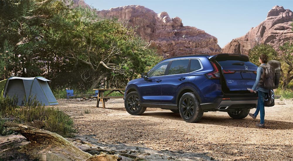 Rear of a blue 2026 Honda CR-V Sport Touring Hybrid parked off-road near a camp.