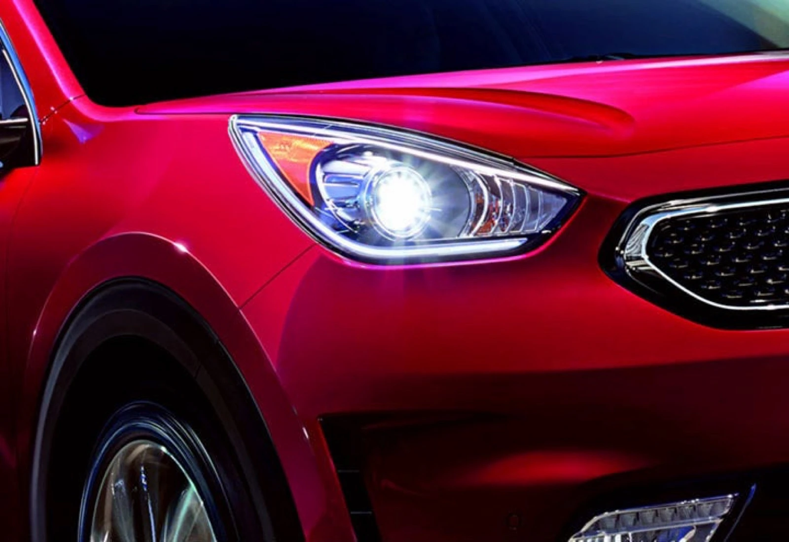 Extreme close-up of a red Kia vehicle's illuminated LED headlight and grille.
